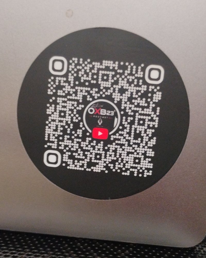 Round black OXB23³ QR code sticker on a laptop lid